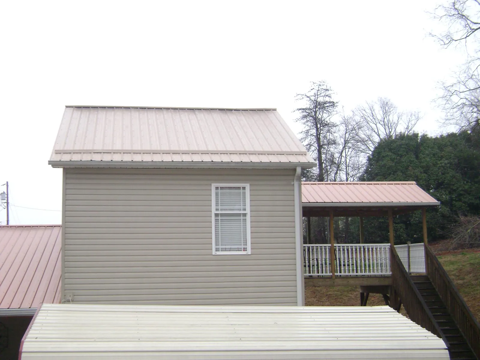 Tan metal roofs on a two story addition and attached porch, from a Roof Replacement job in Linwood